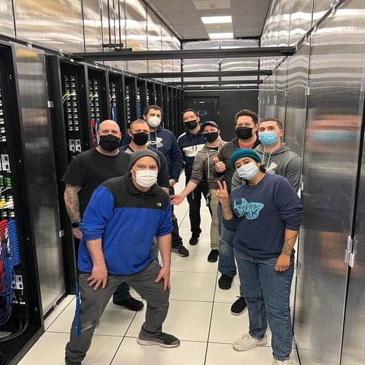 About Expert team solutions of Kurumin Brasil technicians working inside a modern data center in the USA, surrounded by server racks with organized cabling and advanced technology.