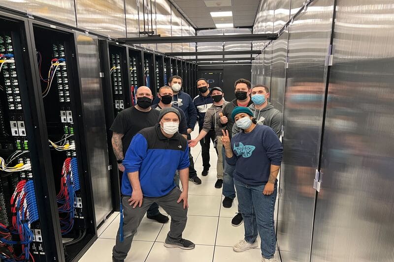Behind the Scenes: Kurumin Brasil Team at a High-Tech Data Center in the USA About Expert team solutions of Kurumin Brasil technicians working inside a modern data center in the USA, surrounded by server racks with organized cabling and advanced technology.