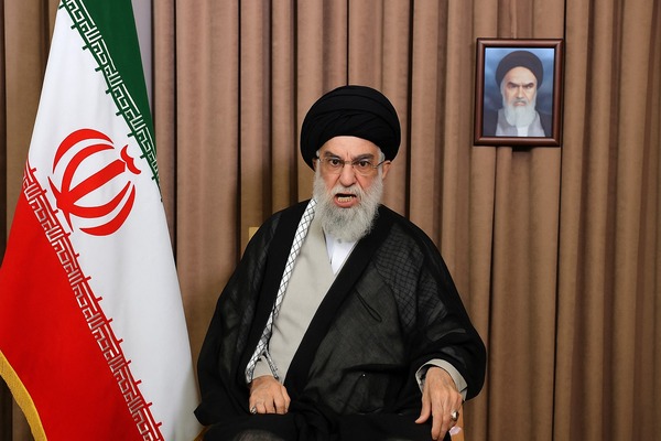 Ayatollah Ali Khamenei looking furious, seated beside Iran's national flag and Khomeini's portrait, symbolizing Iran’s strong response to US and Israeli actions.